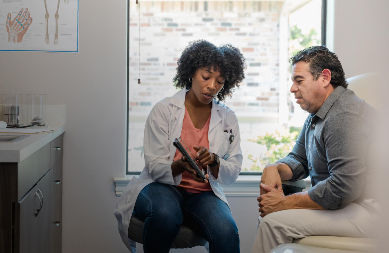 Female doctor and a male patient sitting in a exam room pointing to a tablet
